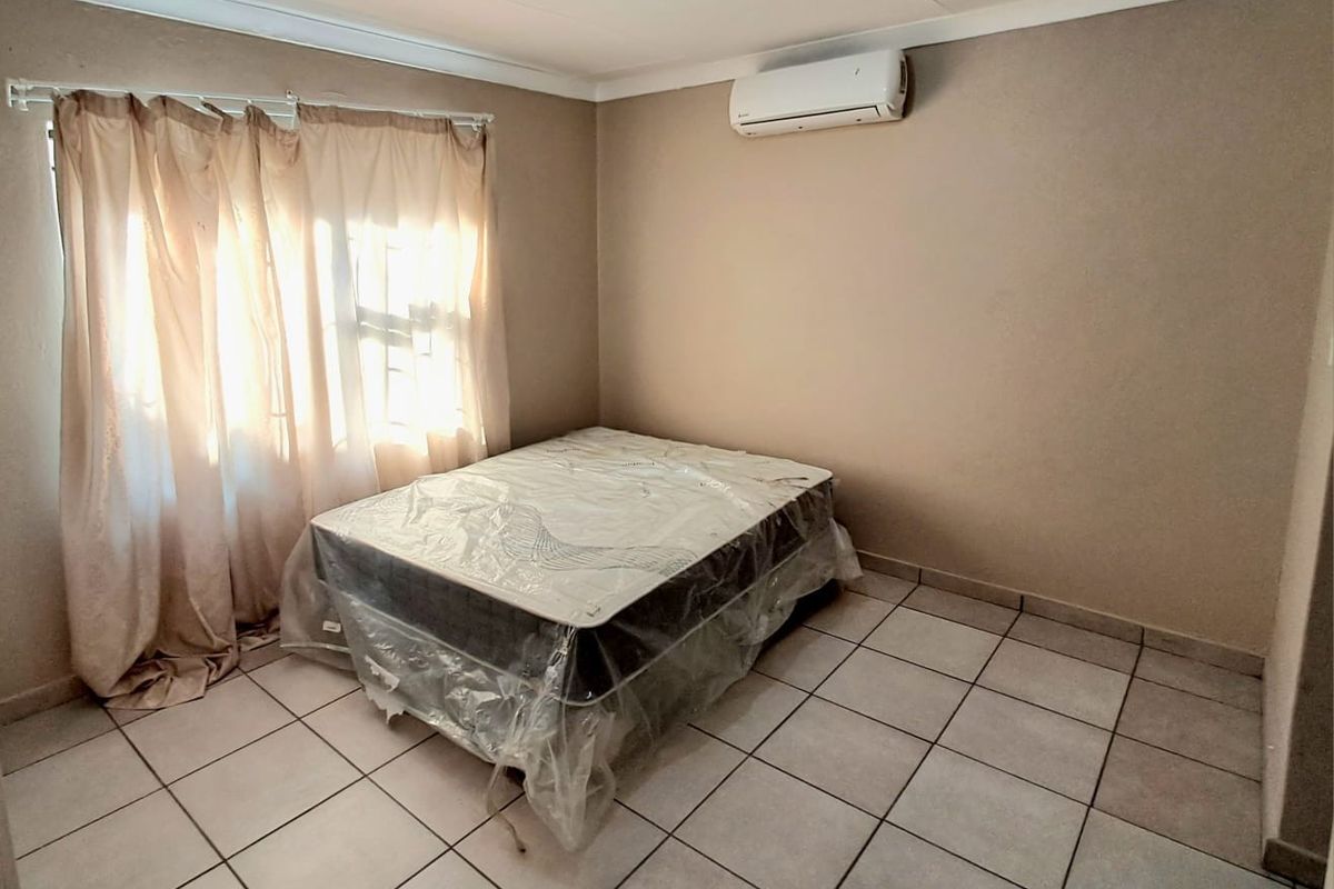 A simple bedroom featuring tiled flooring and a wall-mounted split-system air conditioner.