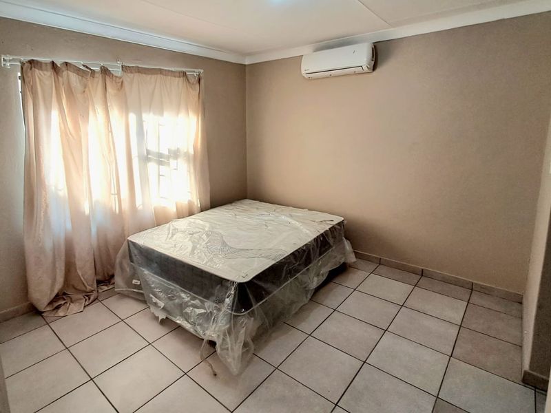A simple bedroom featuring tiled flooring and a wall-mounted split-system air conditioner.