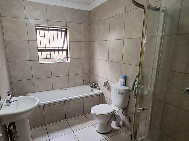 A functional bathroom featuring a pedestal basin, built-in bathtub, toilet, and a curved glass shower enclosure with neutral ceramic tiling throughout.