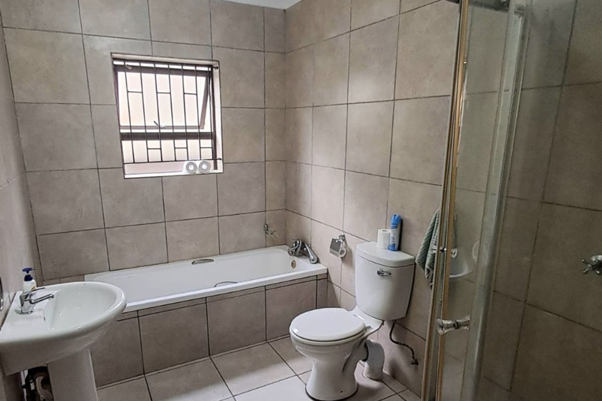 A functional bathroom featuring a pedestal basin, built-in bathtub, toilet, and a curved glass shower enclosure with neutral ceramic tiling throughout.