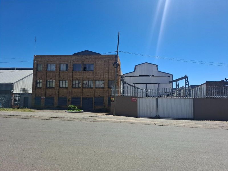 Front elevation of a multi-story industrial building featuring brick facade, secure gated entrance, and industrial roller shutter doors.