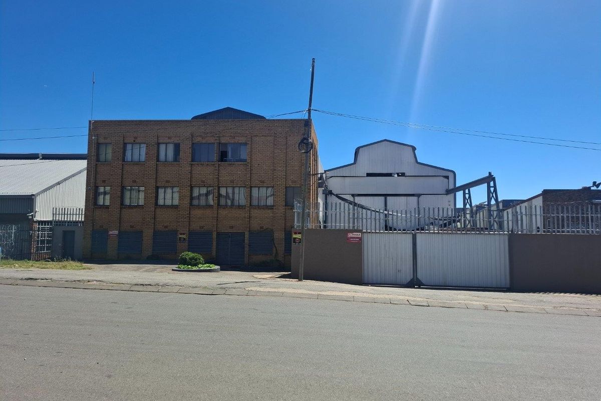 Front elevation of a multi-story industrial building featuring brick facade, secure gated entrance, and industrial roller shutter doors.