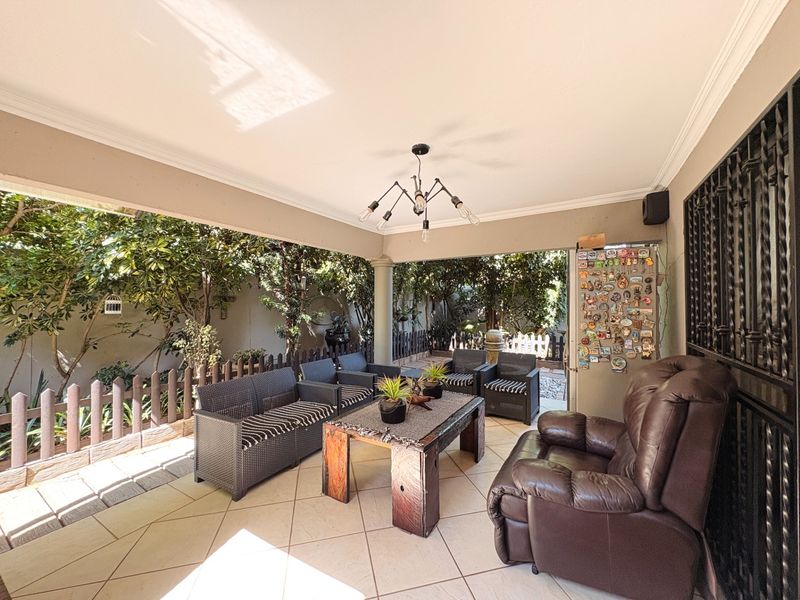 A spacious covered patio featuring tiled flooring and a central light fixture, providing a comfortable outdoor entertainment area overlooking the garden.