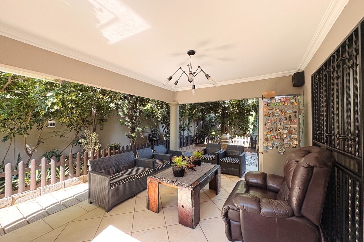A spacious covered patio featuring tiled flooring and a central light fixture, providing a comfortable outdoor entertainment area overlooking the garden.