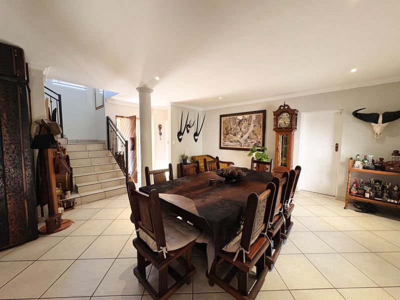 Spacious dining area featuring tiled flooring, a central structural column, and an open-plan staircase with a metal balustrade.