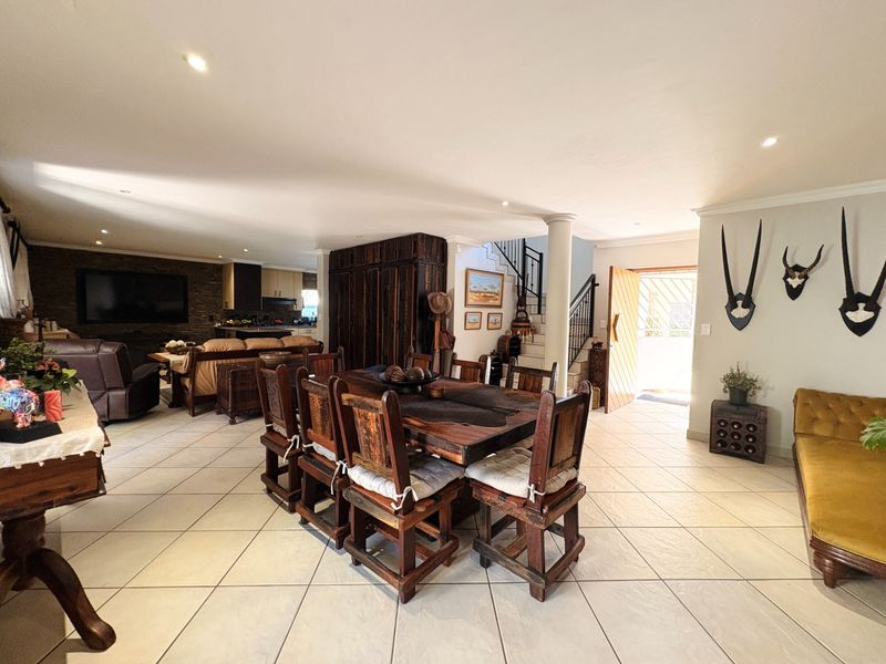 Spacious open-plan living and dining area featuring tiled floors, recessed lighting, a stone feature wall, and a staircase leading to the upper level.