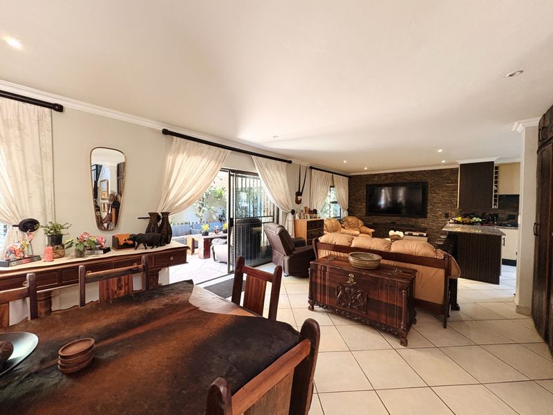 Spacious open-plan living and dining area featuring tiled floors, an exposed brick feature wall, and seamless flow to the outdoor patio through sliding doors.