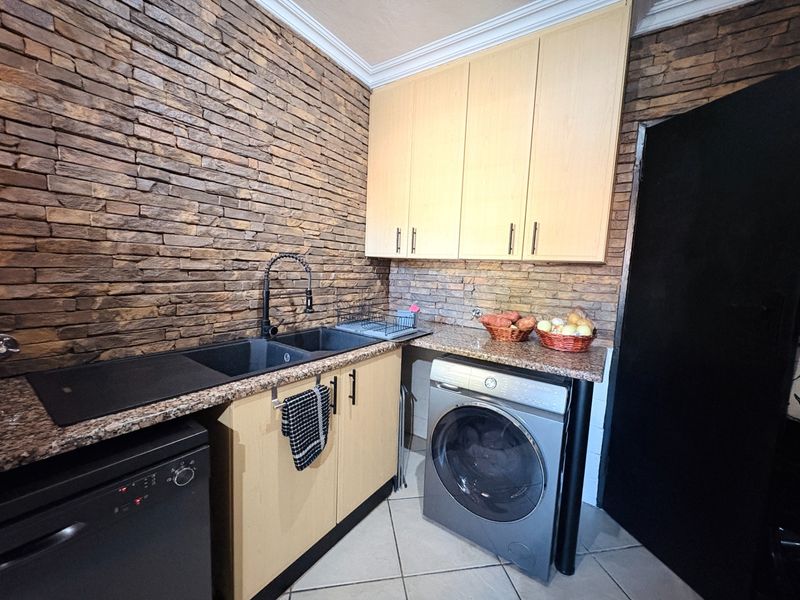 Functional scullery featuring stone veneer wall cladding, granite countertops, double basin sink, and built-in cabinetry with dedicated space for laundry appliances.