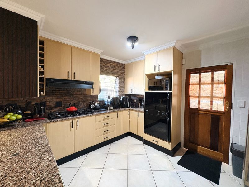Functional kitchen featuring light wood cabinetry, granite countertops, built-in oven, gas hob, and a decorative brick-style backsplash with tiled flooring.