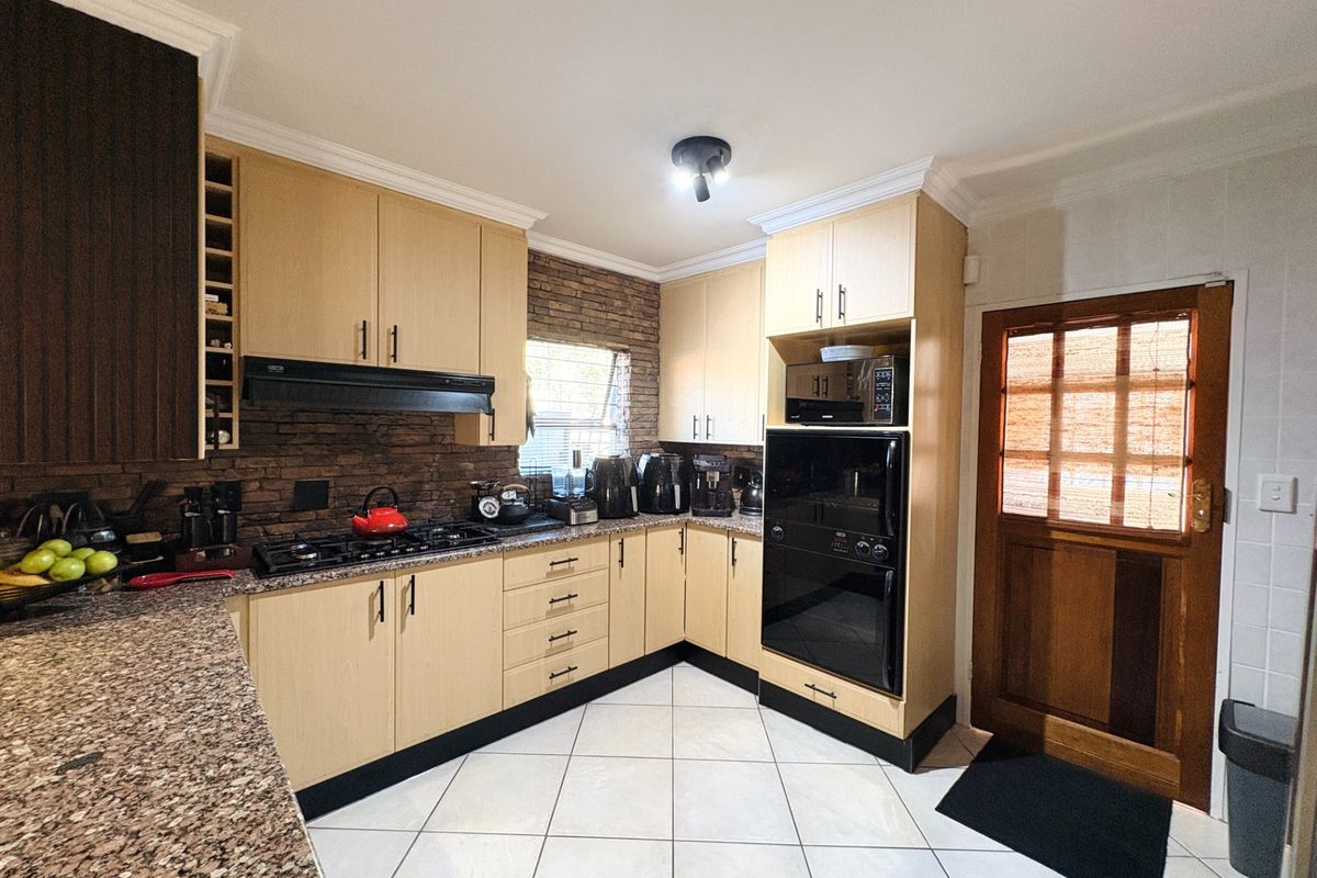 Functional kitchen featuring light wood cabinetry, granite countertops, built-in oven, gas hob, and a decorative brick-style backsplash with tiled flooring.