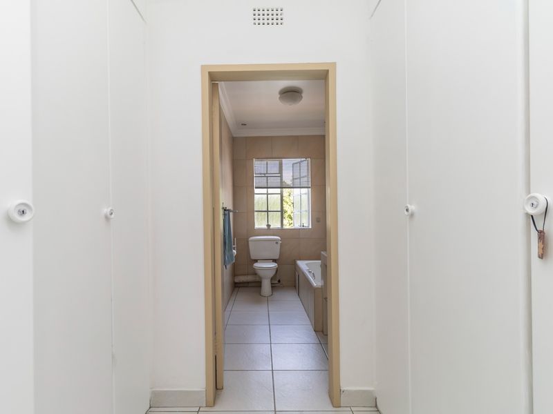 A view through a hallway with built-in storage cupboards into a functional bathroom featuring a toilet, bathtub, and tiled finishes.