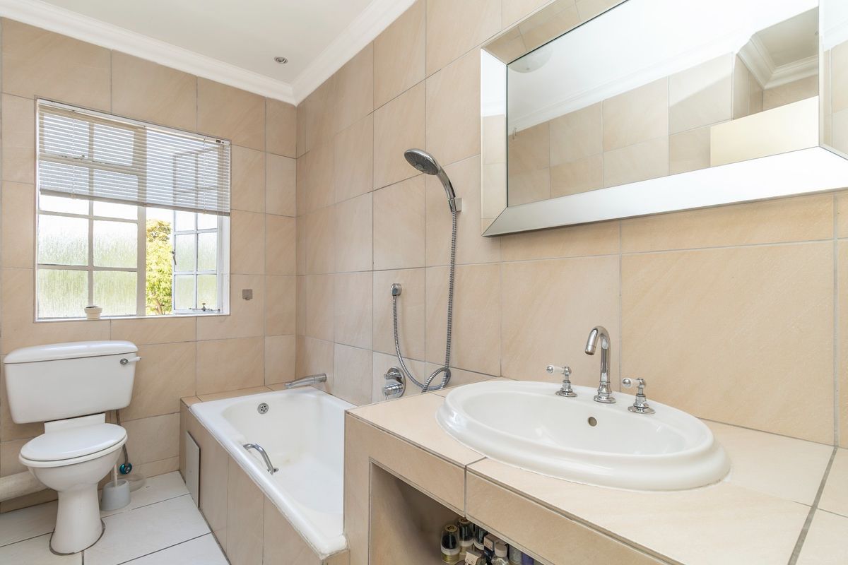 A clean, neutral-toned bathroom featuring a built-in bathtub, vanity basin, and tiled finishes throughout, offering a functional and well-maintained space.