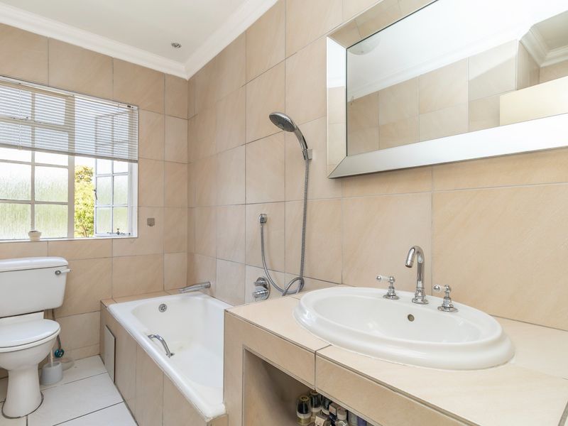 A clean, neutral-toned bathroom featuring a built-in bathtub, vanity basin, and tiled finishes throughout, offering a functional and well-maintained space.