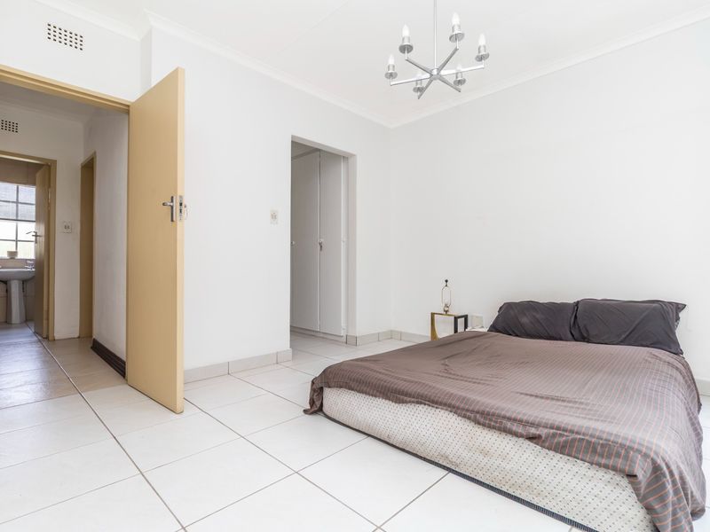 A bedroom featuring tiled flooring, built-in cupboards, and a ceiling light fixture, with an adjacent view into a bathroom area.