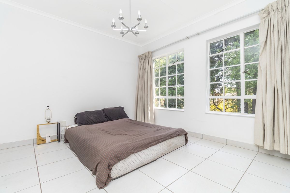 A bright bedroom featuring large multi-pane windows, tiled flooring, and a central ceiling light fixture, offering a clean and neutral space.