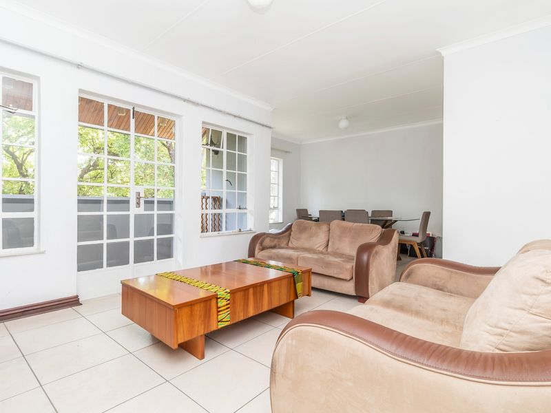 Spacious open-plan living and dining area featuring neutral tiled flooring, large windows, and classic french doors leading to an outdoor space.