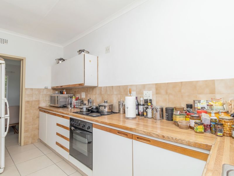 A functional kitchen featuring built-in cabinetry, a laminate countertop, tiled backsplash, and integrated oven and hob, offering a practical layout for daily use.
