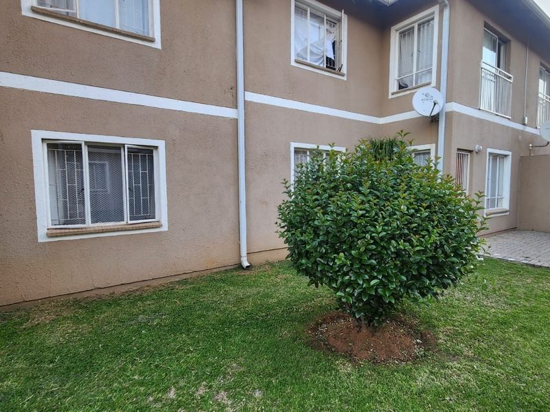Rear view of the apartment building featuring a small private garden area with a paved walkway and security bars on the windows.
