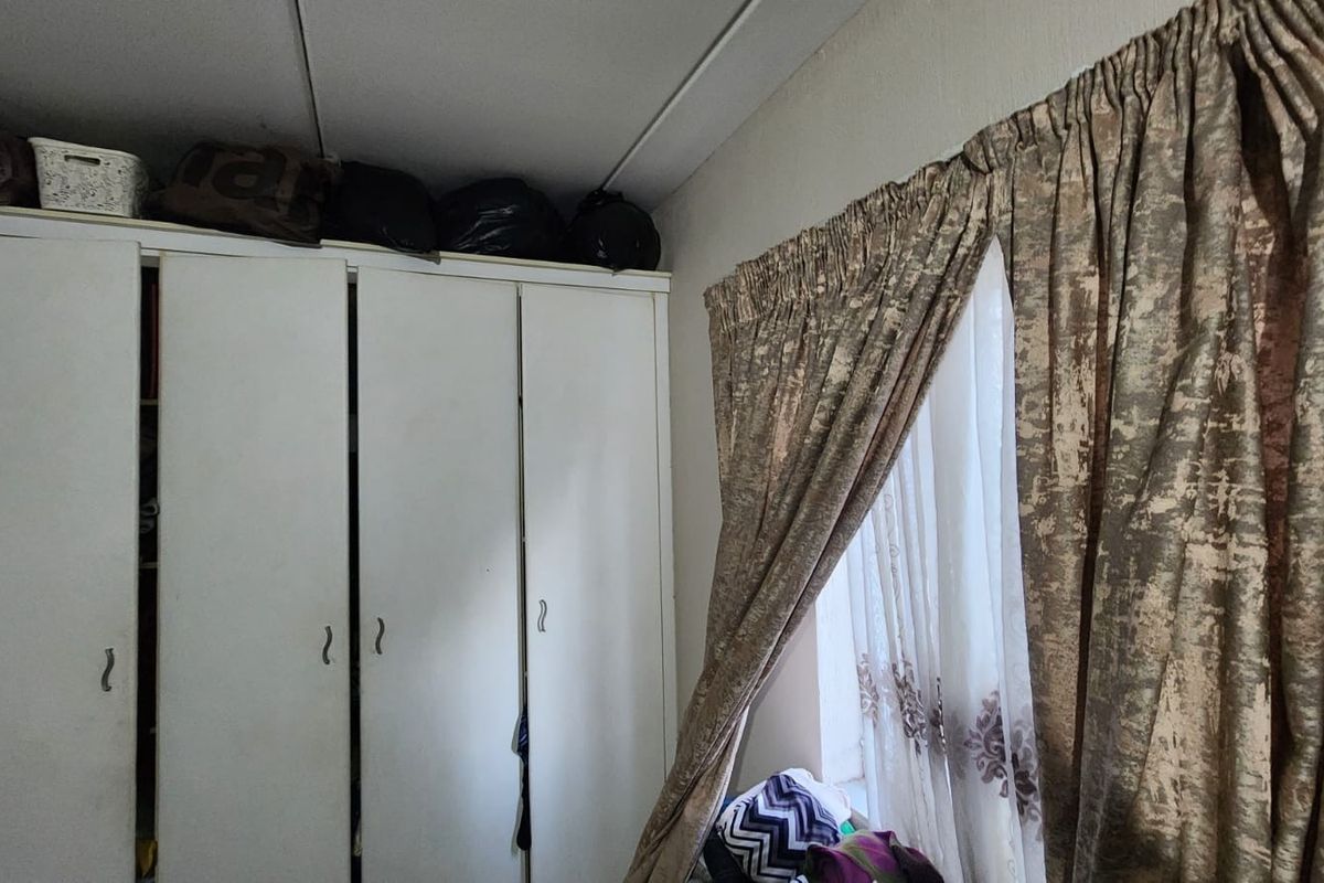 A bedroom featuring a white built-in wardrobe and window with curtains.
