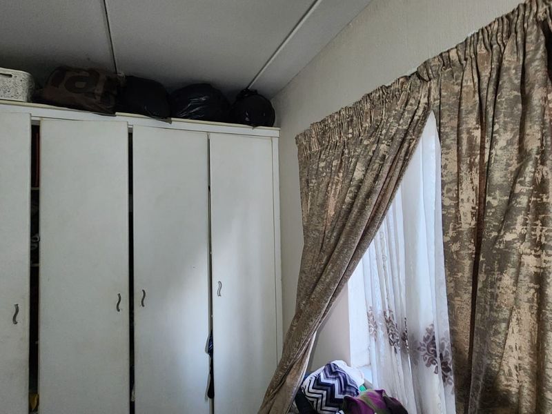 A bedroom featuring a white built-in wardrobe and window with curtains.