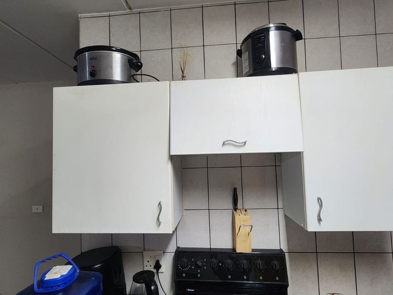 A functional kitchen area featuring white wall-mounted cabinetry and a tiled backsplash above a freestanding stove.