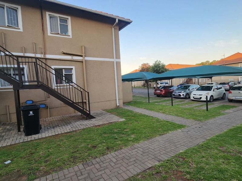Exterior view of the apartment building featuring a metal staircase, paved walkways, and covered parking bays for residents.