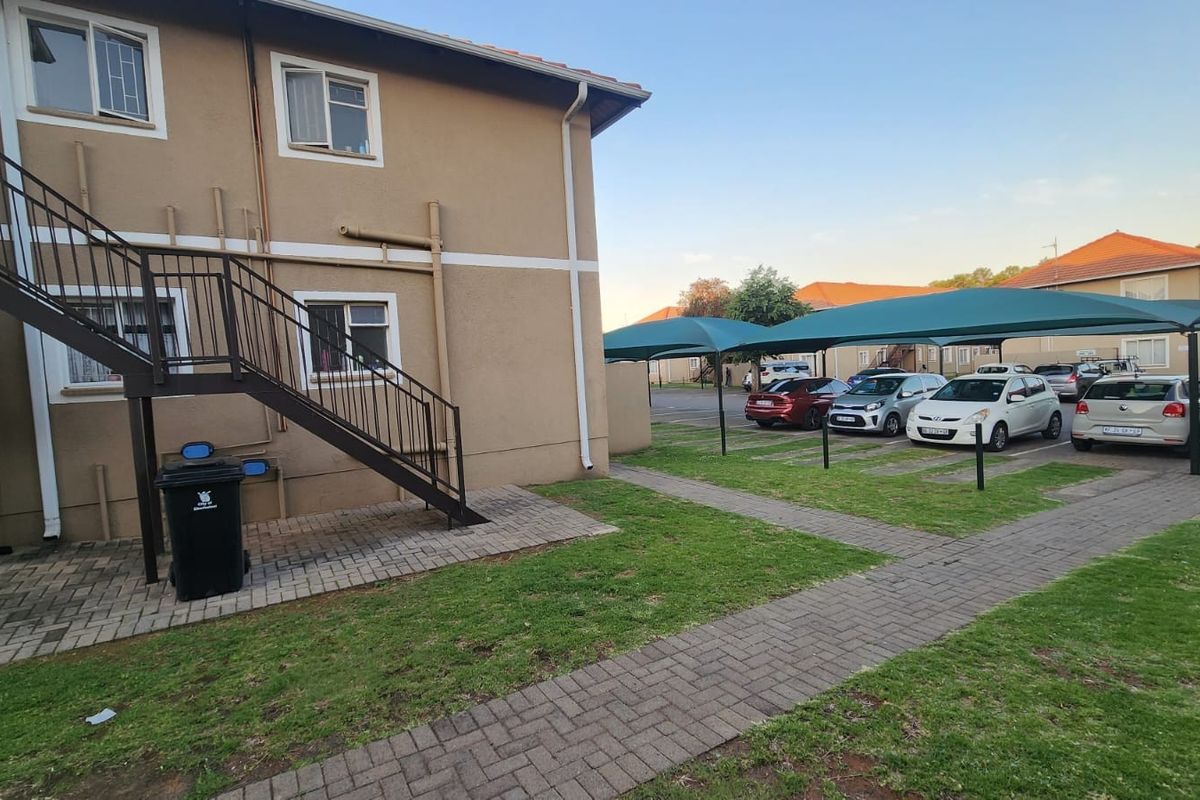 Exterior view of the apartment building featuring a metal staircase, paved walkways, and covered parking bays for residents.