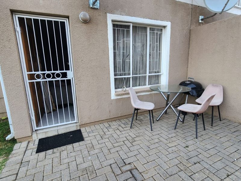 A paved outdoor patio area featuring a security gate entrance and a sliding window, providing a functional space for outdoor relaxation.