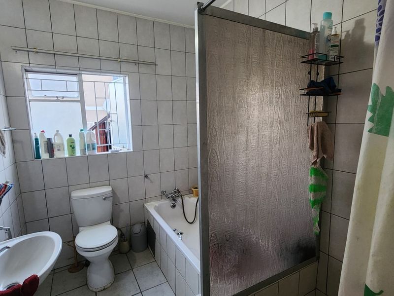 A functional bathroom featuring a bathtub with a shower screen, pedestal basin, and toilet, finished with full-height wall tiling.