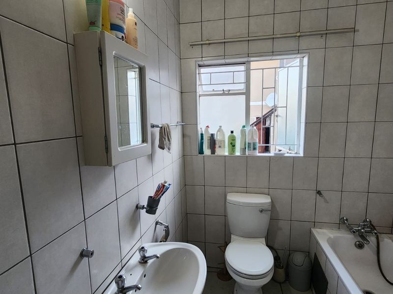 A functional bathroom featuring tiled walls and floors, a pedestal basin, a standard toilet, and a bathtub with a handheld shower attachment.