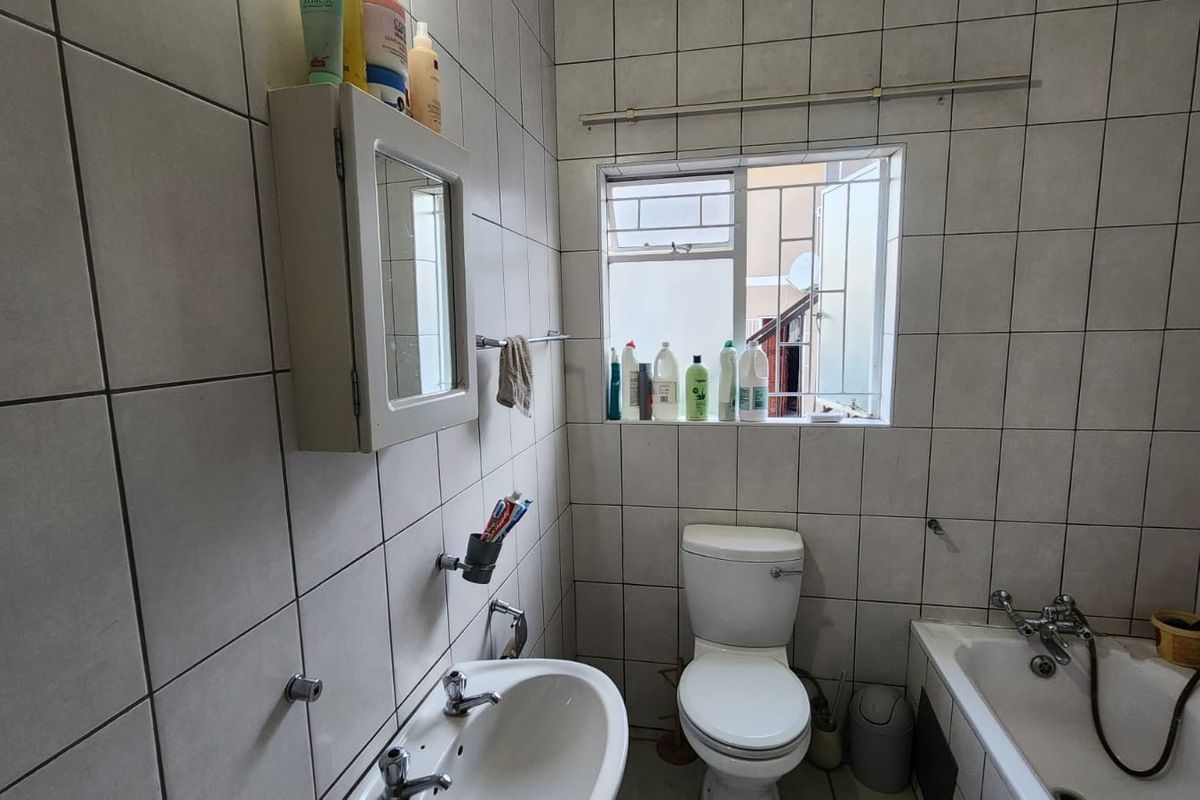 A functional bathroom featuring tiled walls and floors, a pedestal basin, a standard toilet, and a bathtub with a handheld shower attachment.