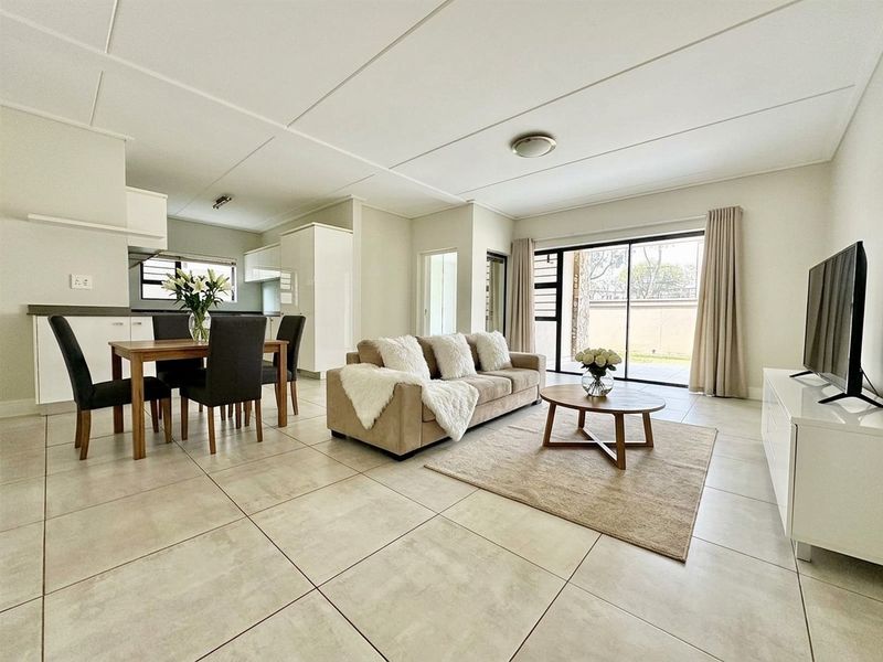 A bright open-plan living and dining area featuring large format floor tiles, modern kitchen cabinetry, and sliding glass doors leading to the exterior.