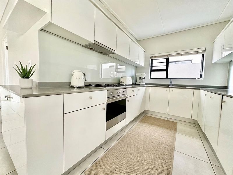 Modern kitchen featuring sleek white cabinetry, stone countertops, integrated gas hob, built-in oven, and a glass splashback with tiled flooring.