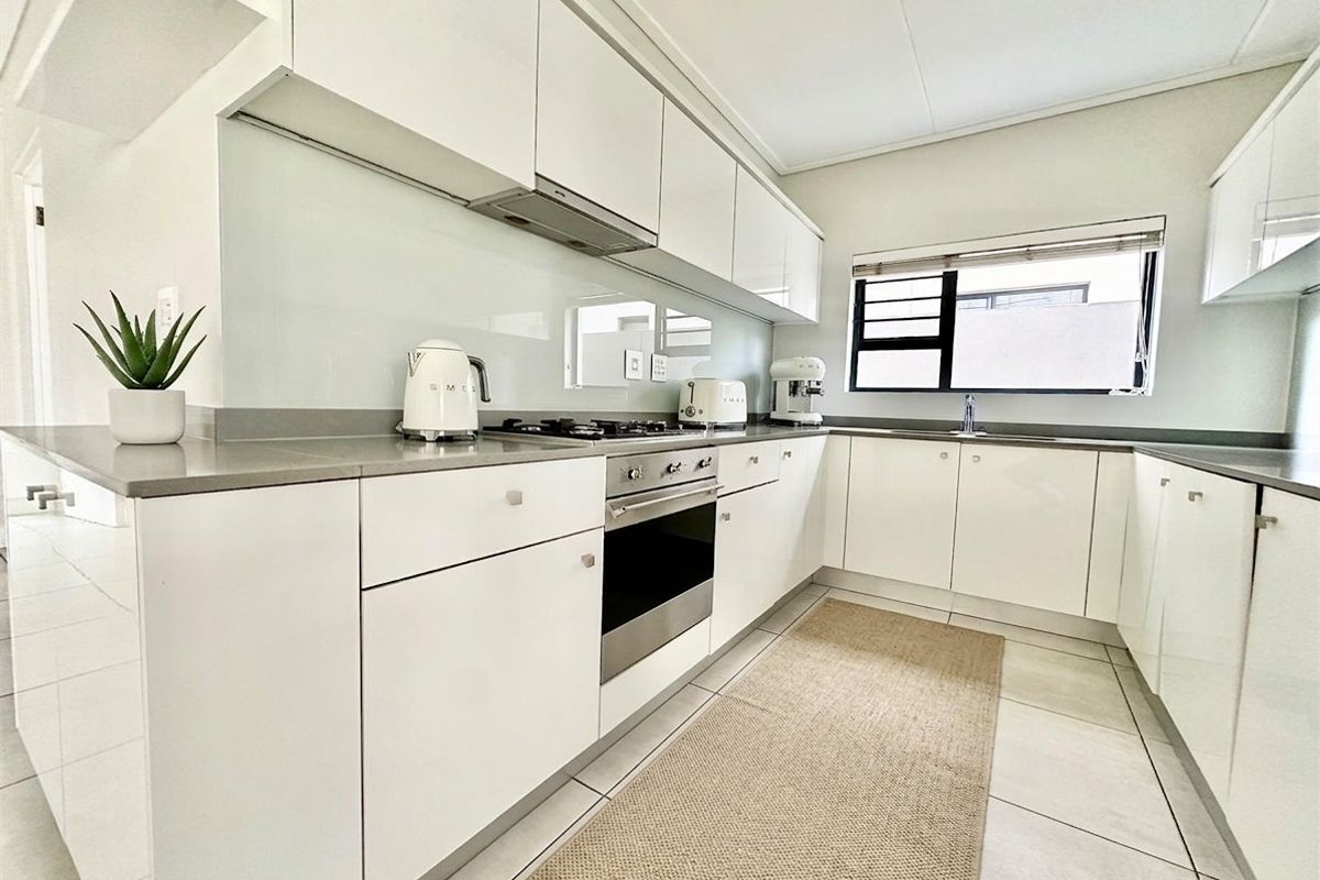 Modern kitchen featuring sleek white cabinetry, stone countertops, integrated gas hob, built-in oven, and a glass splashback with tiled flooring.