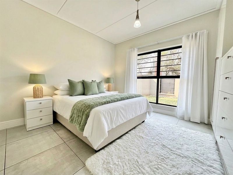 A bright and well-maintained bedroom featuring tiled flooring, a built-in wardrobe, and a large window with security bars overlooking the exterior.