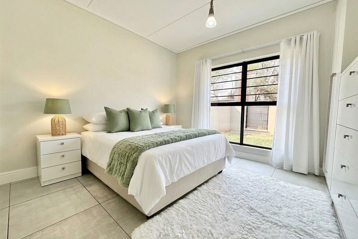 A bright and well-maintained bedroom featuring tiled flooring, a built-in wardrobe, and a large window with security bars overlooking the exterior.