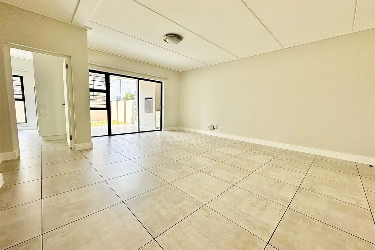 A bright, empty living room featuring neutral tiled flooring, clean walls, and a sliding glass door providing access to the outdoor area.