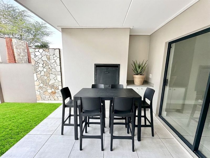 A modern covered patio featuring a built-in braai, stone cladding detail, and large sliding glass doors leading to the interior.