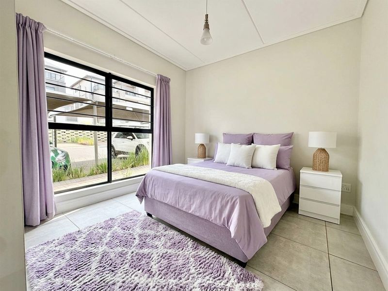 A bright and well-maintained bedroom featuring large aluminium-framed windows, neutral tiled flooring, and a clean, modern aesthetic.
