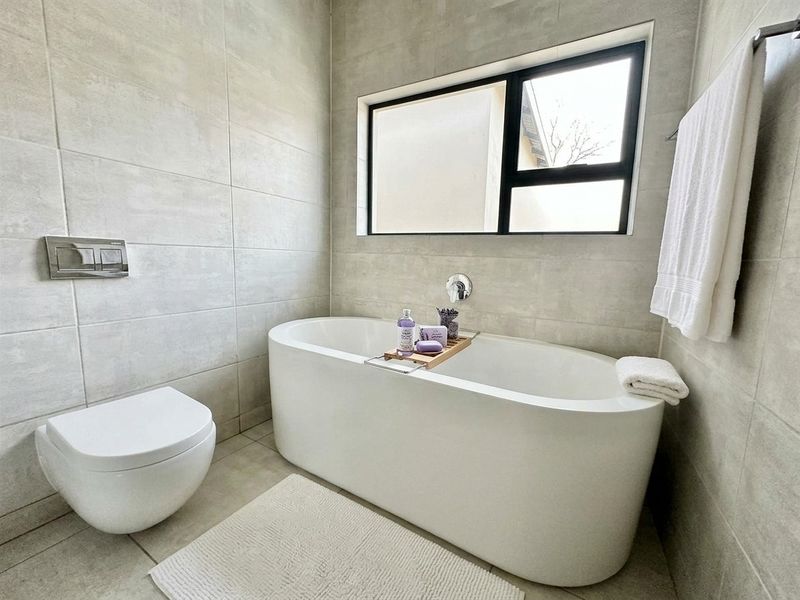 Modern bathroom featuring a sleek freestanding bathtub, wall-mounted toilet with concealed cistern, and neutral large-format wall tiles.