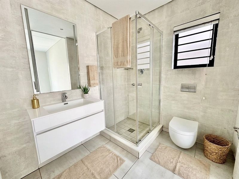Modern bathroom featuring a wall-mounted vanity with integrated basin, glass shower enclosure, and wall-hung toilet with concealed cistern, finished with neutral floor-to-ceiling tiles.