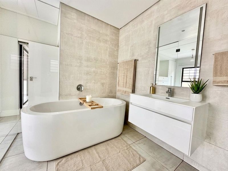 Modern bathroom featuring a sleek freestanding bathtub, wall-mounted faucet, and a contemporary floating vanity with an integrated sink and large mirror.