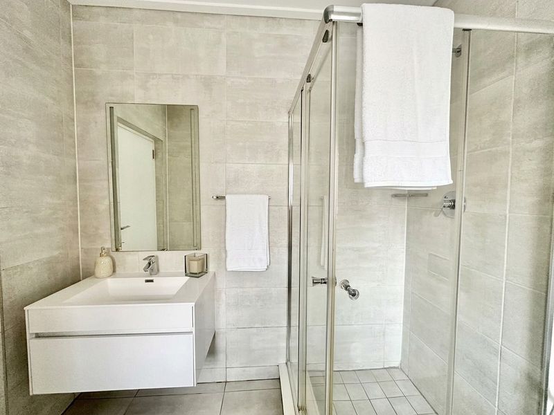 Modern bathroom featuring a wall-mounted vanity with integrated basin, chrome fixtures, and a glass-enclosed shower with neutral wall and floor tiling.