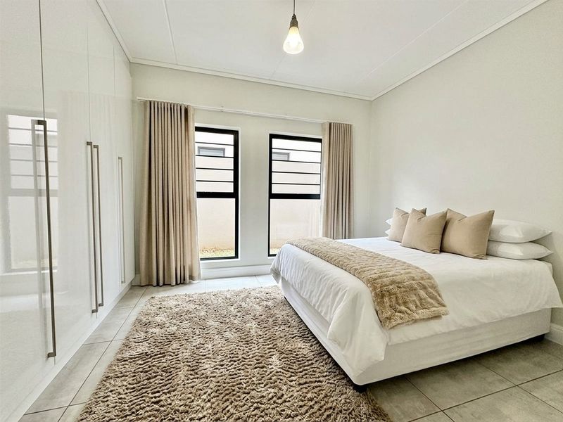 A bright and modern bedroom featuring sleek built-in cupboards, neutral tiled flooring, and large windows that provide ample natural light.