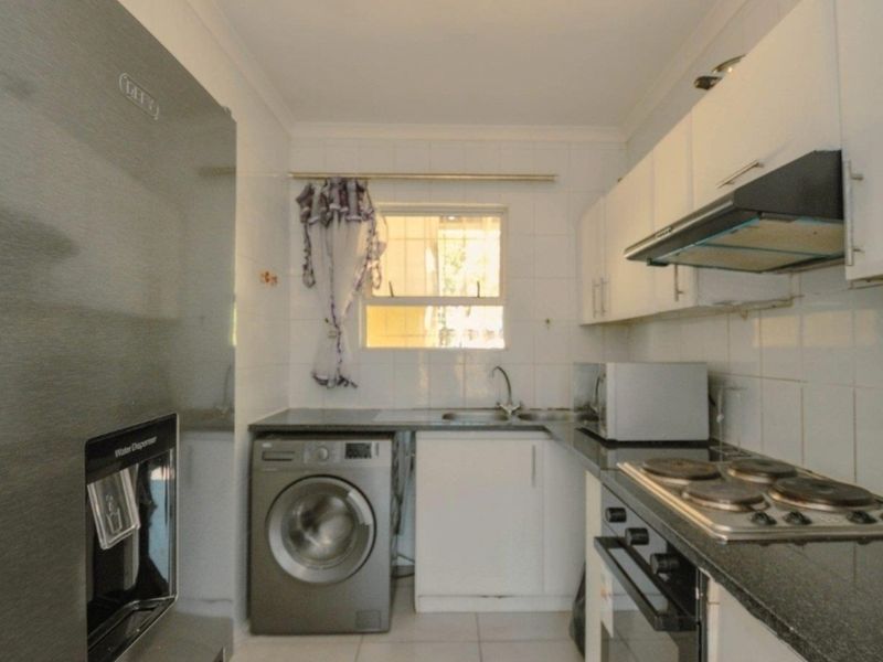 Compact kitchen featuring built-in cabinetry, granite countertops, integrated oven and hob, extractor fan, and tiled finishes with space for laundry appliances.