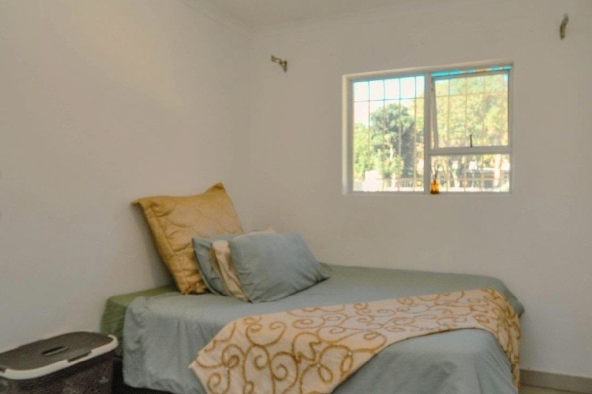 A simple bedroom featuring tiled flooring and a window fitted with security bars.