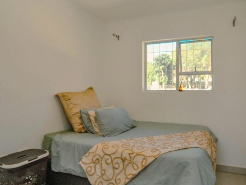 A simple bedroom featuring tiled flooring and a window fitted with security bars.