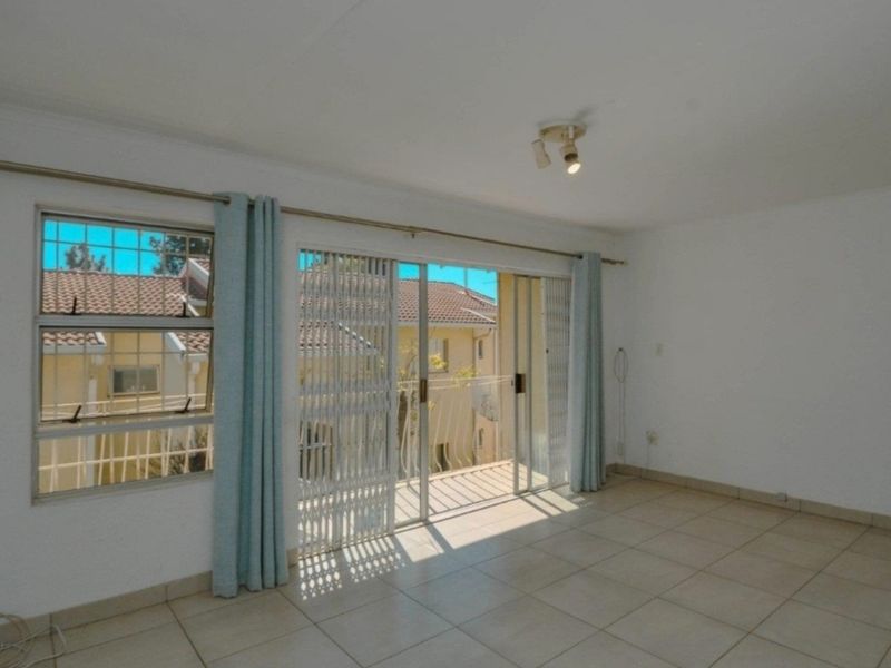 A bright, empty living room featuring tiled flooring, a ceiling light fixture, and a sliding glass door providing access to a balcony.