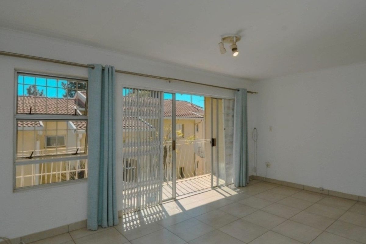 A bright, empty living room featuring tiled flooring, a ceiling light fixture, and a sliding glass door providing access to a balcony.