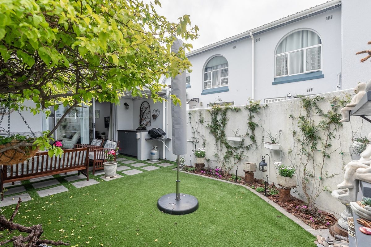 A private rear courtyard featuring an artificial lawn, paved patio area, and a built-in outdoor counter, set against the townhouse rear elevation.